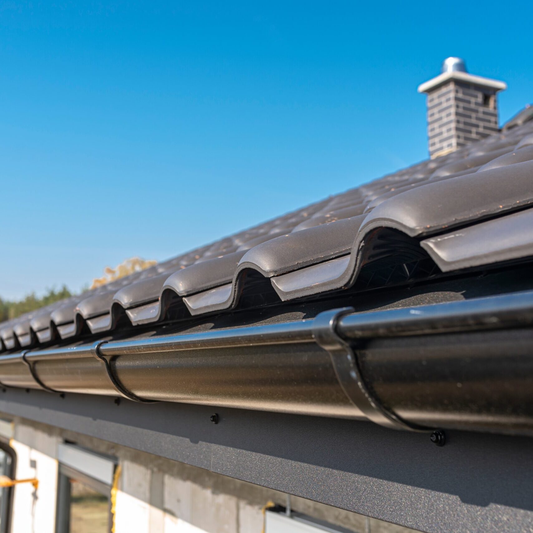 a-metal-black-gutter-on-a-roof-covered-with-ceram-2022-11-10-18-00-38-utc