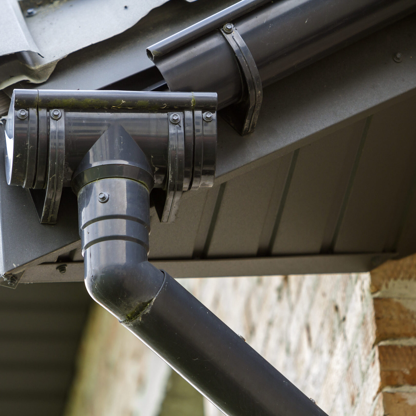 Close-up detail image of a corner of new built brick cottage house roof with steel gutter rain system. Professional construction and drainage pipes installation and connection concept.