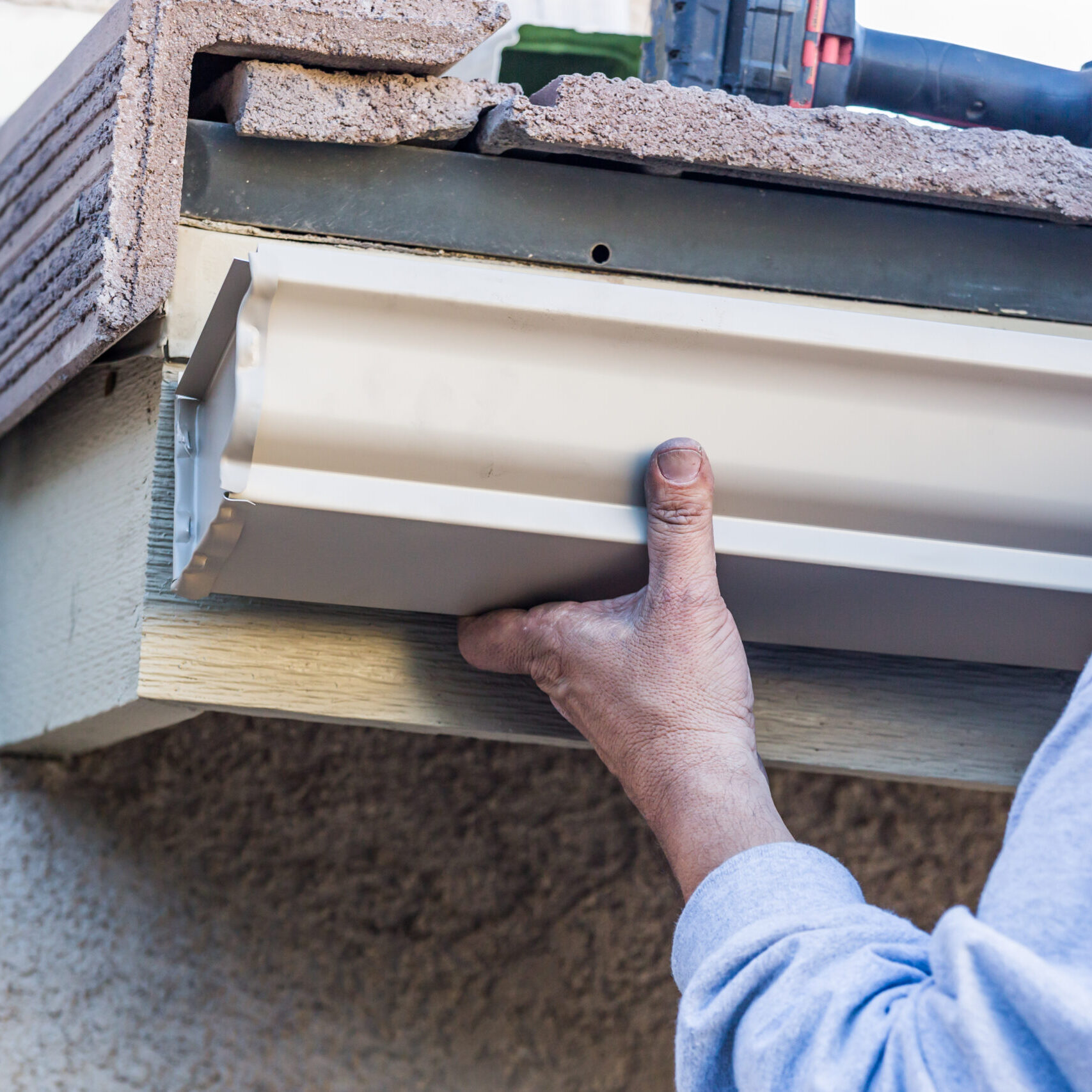 Worker Attaching Aluminum Rain Gutter to Fascia of House.